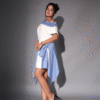 Woman wearing a stylish off-shoulder white shirt dress with blue ruffle neckline and striped asymmetrical wrap skirt, posing in black heels.