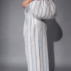 Woman holding a large slouchy striped cotton shoulder bag in neutral and blue tones, styled with matching striped wide-leg pants.